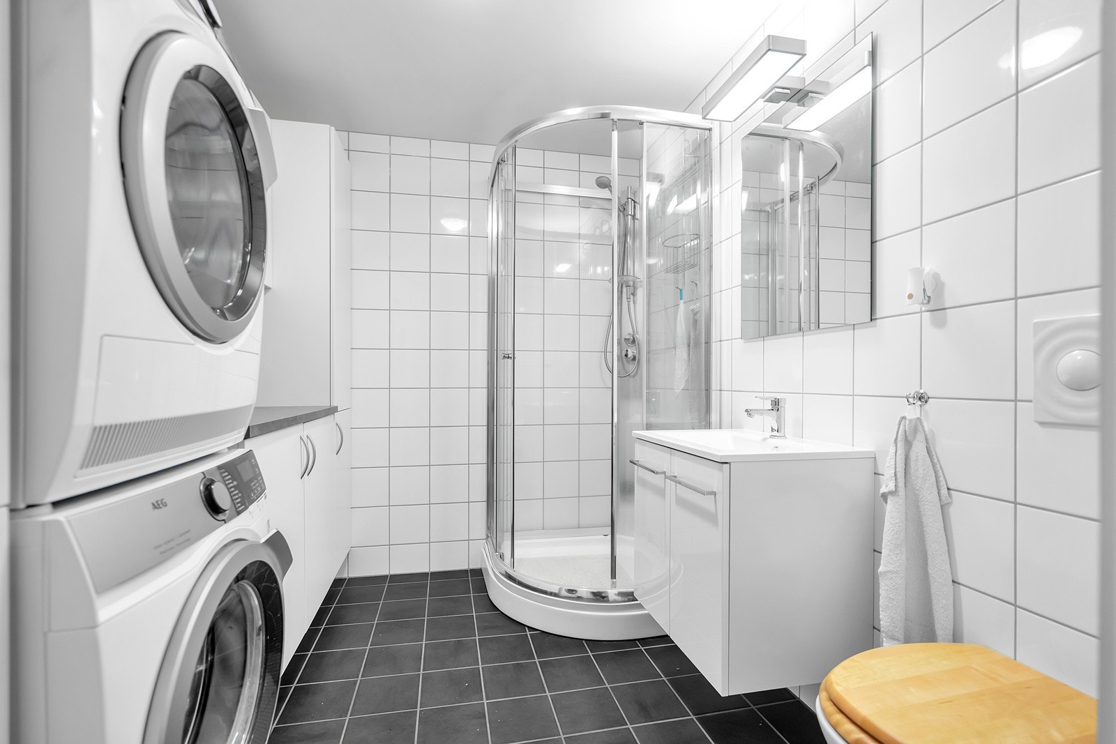 Flislagt bad med dusjkabinett, servantinnredning og opplegg for vaskemaskin og tørketrommel. Galleribilde