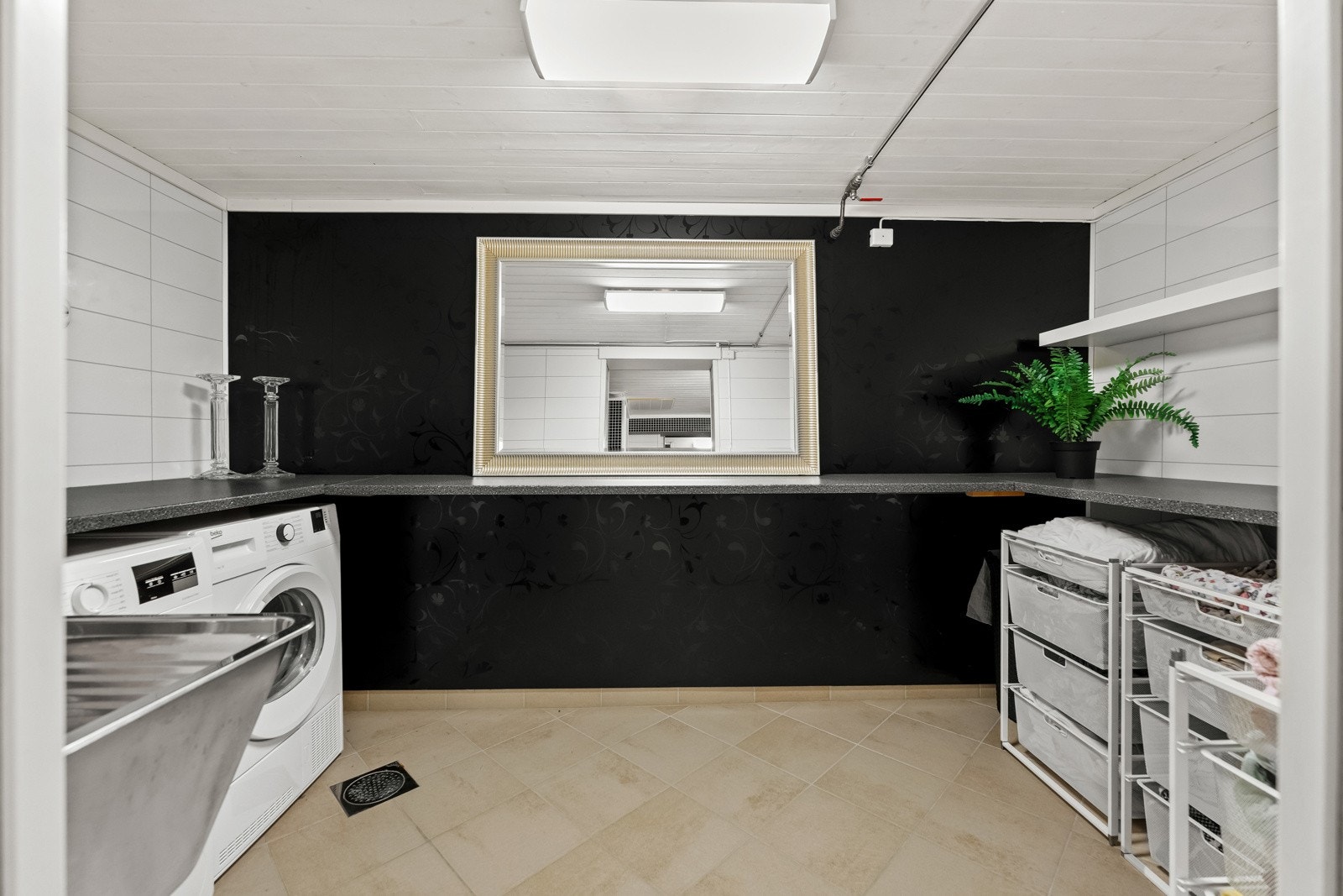 Vaskerom med vaskemaskin, vask, speil og oppbevaringshyller. Lyse vegger og gulvfliser. Galleribilde