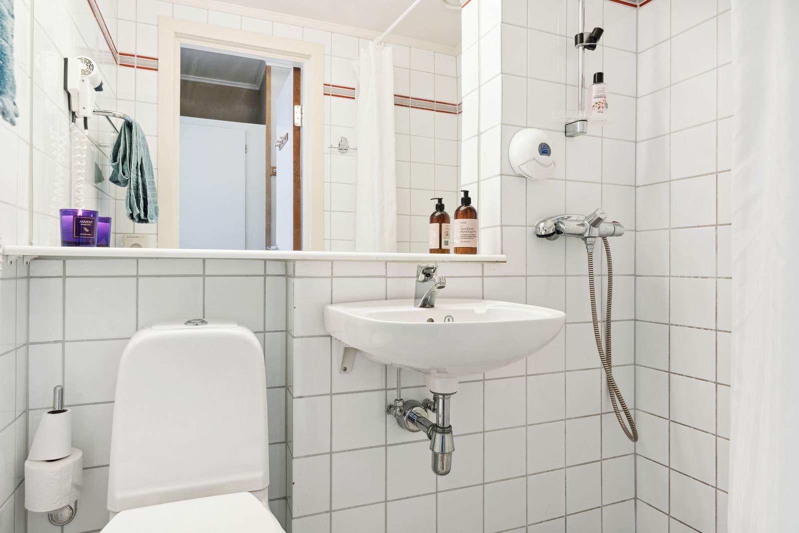 Bad 1 med flisbelagt overflater med varmekabler i gulv. Montert vegghengt porselenservant, gulvstående toalett, vegghengt speil og åpen dusj i hjørne. Galleribilde