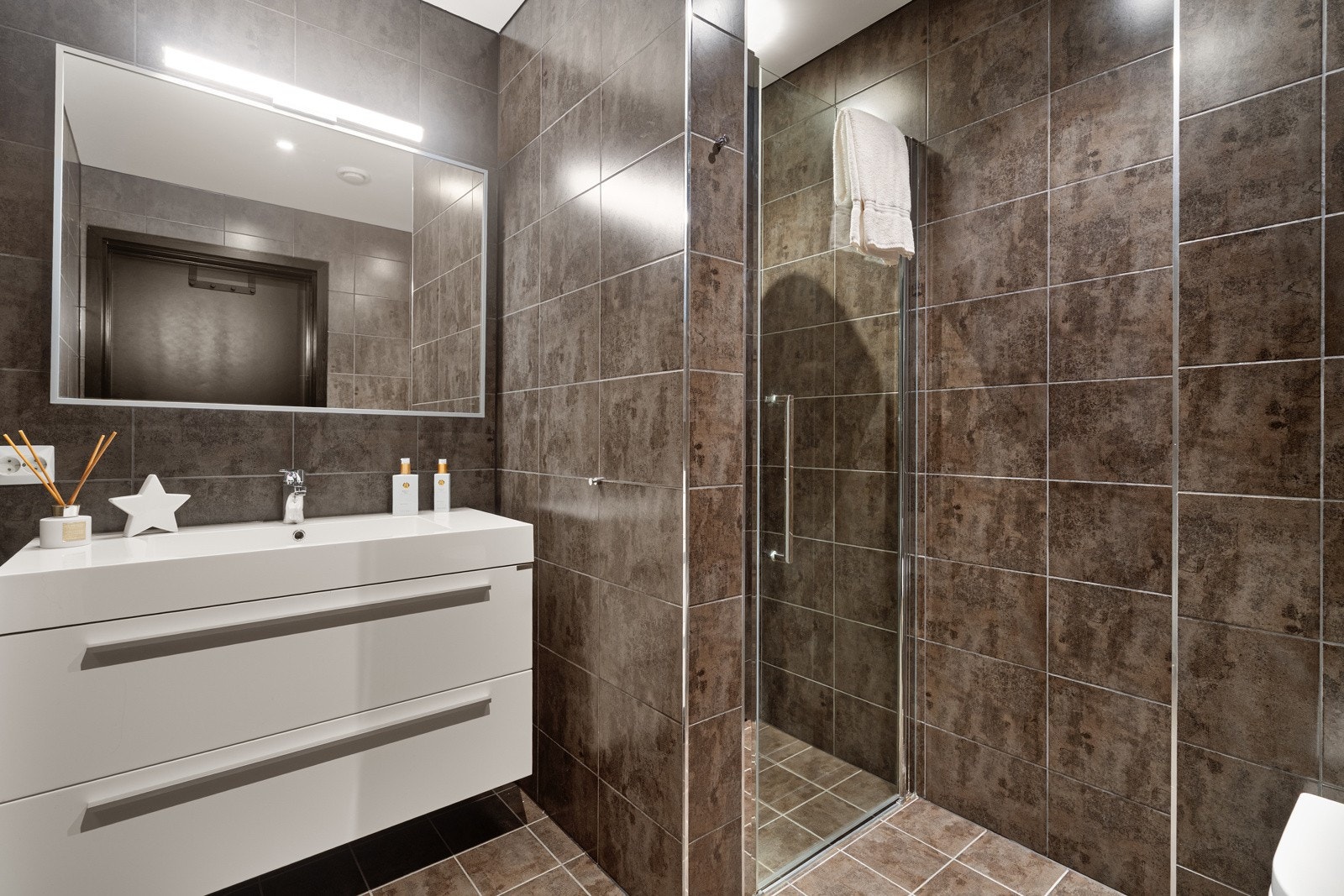 Badet i første etasje er helfliset med vannbåren gulvvarme, moderne innredning, dusjnisje med glassdører og vegghengt toalett. Galleribilde