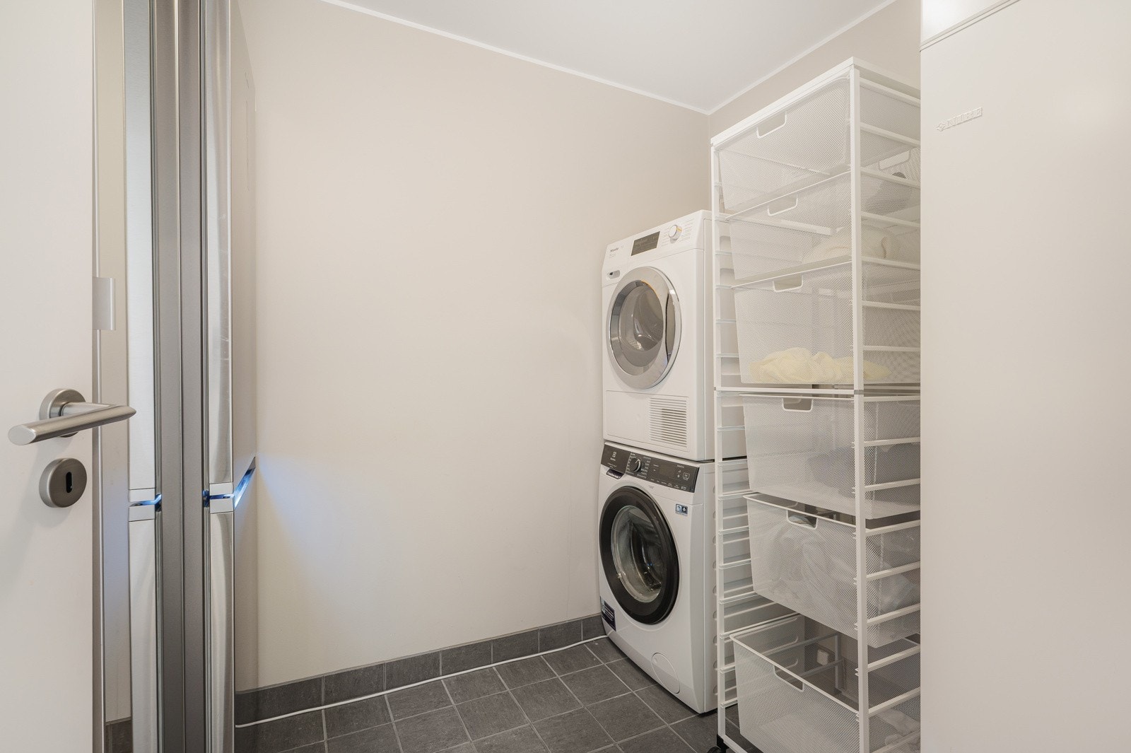 Praktisk vaskerom som måler 5,2 kvadratmeter. Rommet har keramiske fliser på gulv og malt platekledning på vegger og tak. Det er opplegg for vaskemaskin og varmekabler i gulvet. Galleribilde