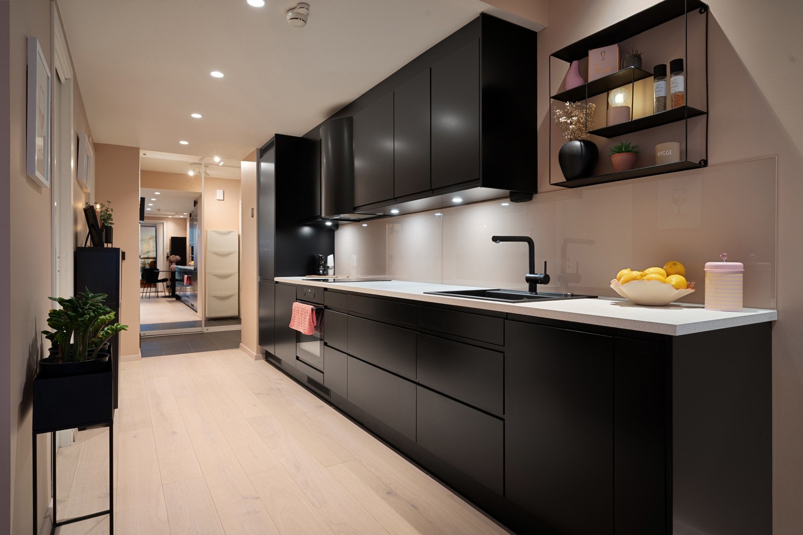 Lekkert kjøkken med slette fronter, glassplater på vegg over benk og belysning under overskap. Galleribilde