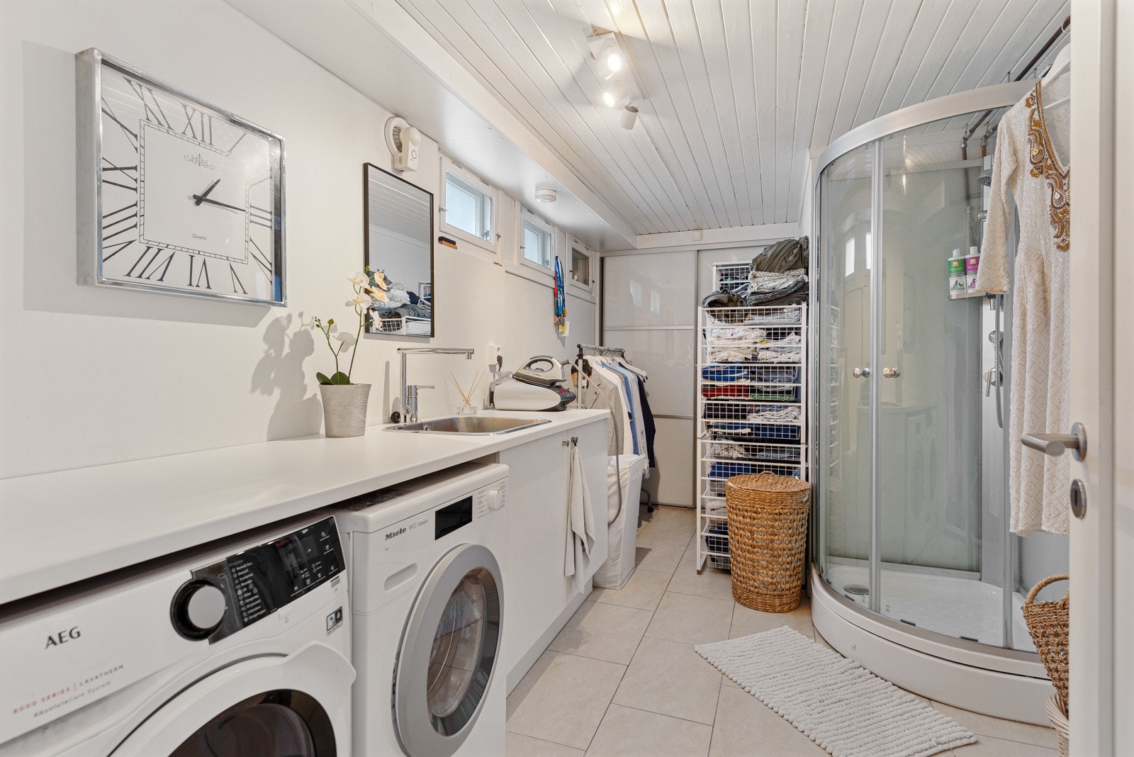 Vaskerom med fliser og vannbåren gulvvarme, med dusjkabinett, benkeskap og opplegg for vaskemaskin og tørketrommel Galleribilde