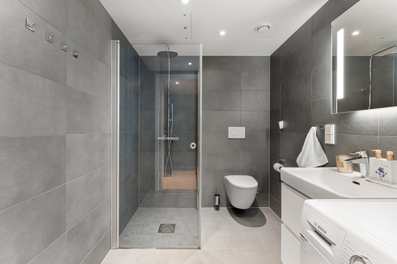 Badet holder en gjennomført standard med flislagt gulv med gulvvarme. flislagte vegger og nedsenket himling med downlights Galleribilde