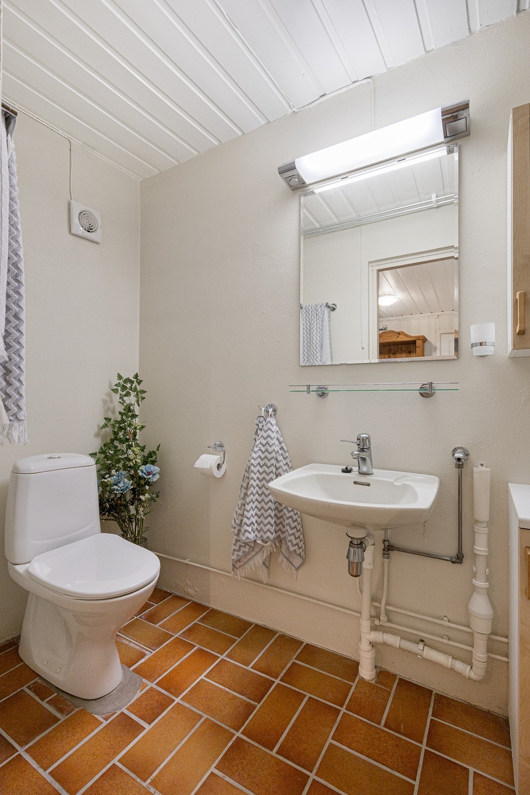 Badet i hybelleiligheten har lysmalte vegger og terracottafargede fliser på gulvet med sluk. Galleribilde