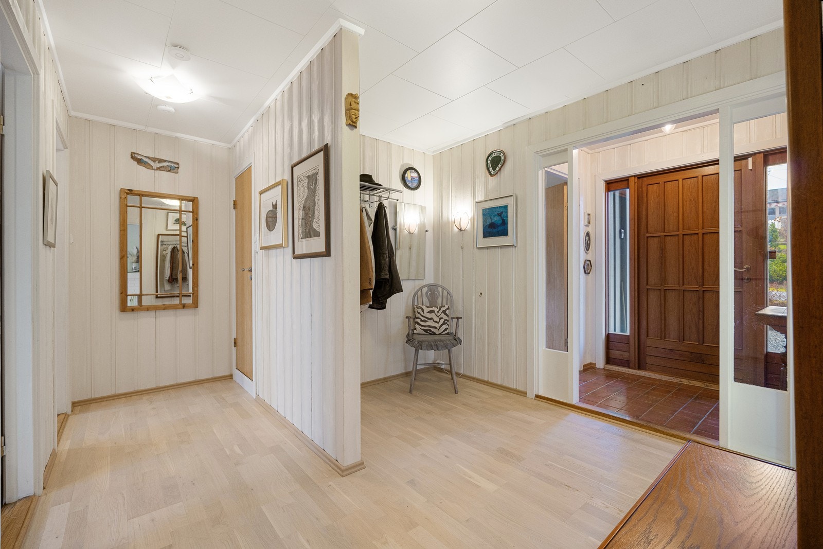 Vel inne er det en lys og tiltalende entré med fliser på gulvet og lysmalt panel på veggene. Videre inn er det en større gang med god plass til garderobeløsninger. Galleribilde