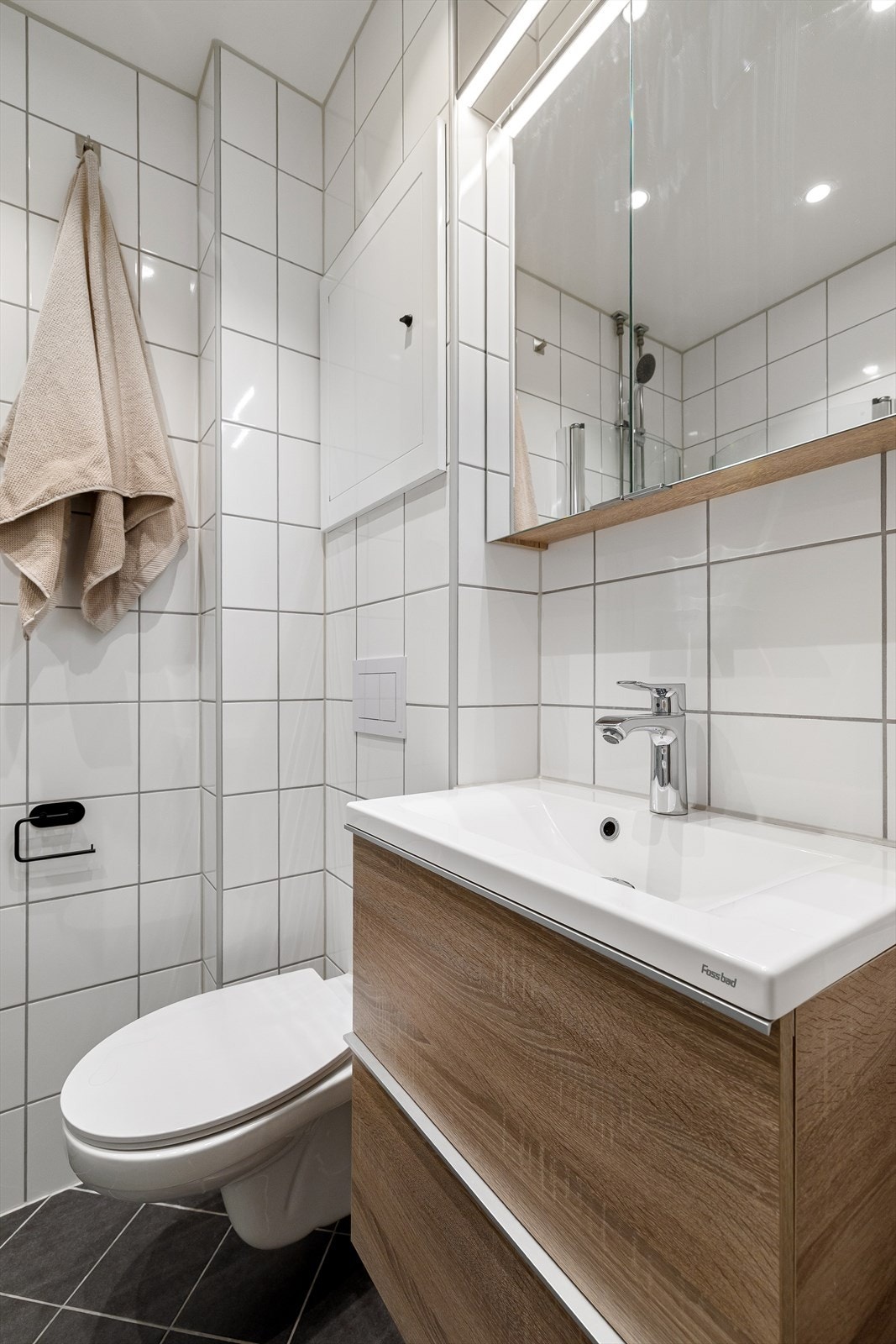 Innredet med vegghengt toalett og en moderne baderomsinnredning. Speilskap med belysning og dusjhjørne med plassbesparende foldedører Galleribilde