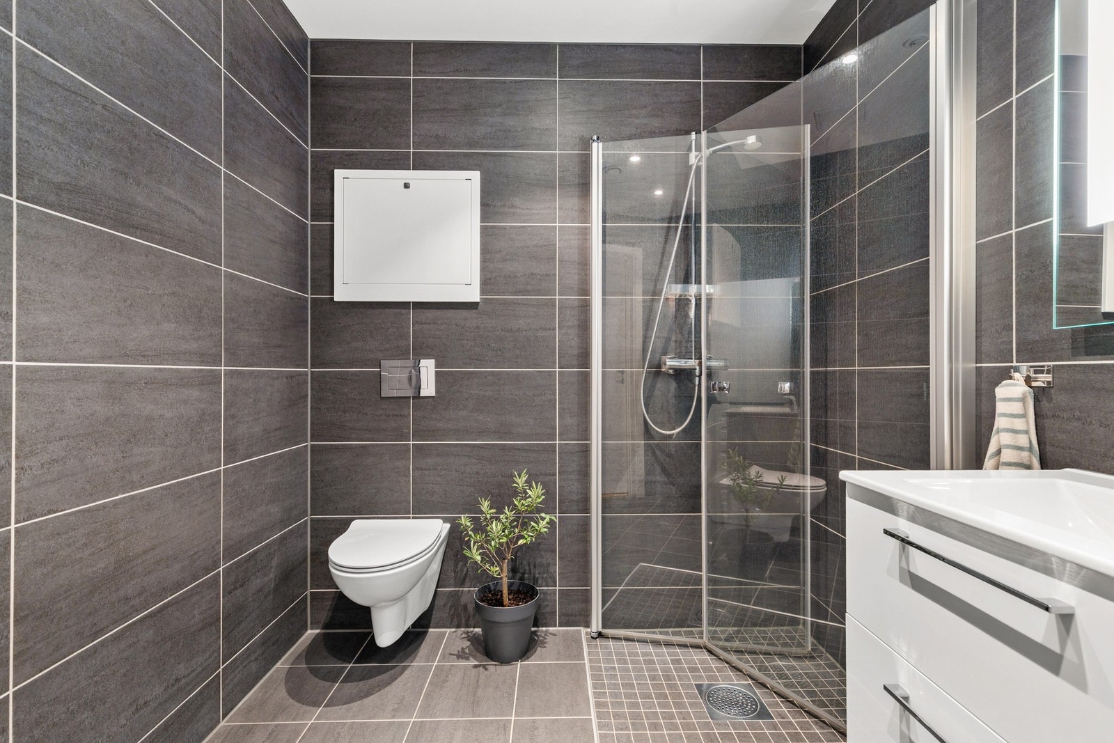 Romslig og helfliset bad innredet med vegghengt toalett, dusjhjørne med innfellbare vegger og servantinnredning Galleribilde