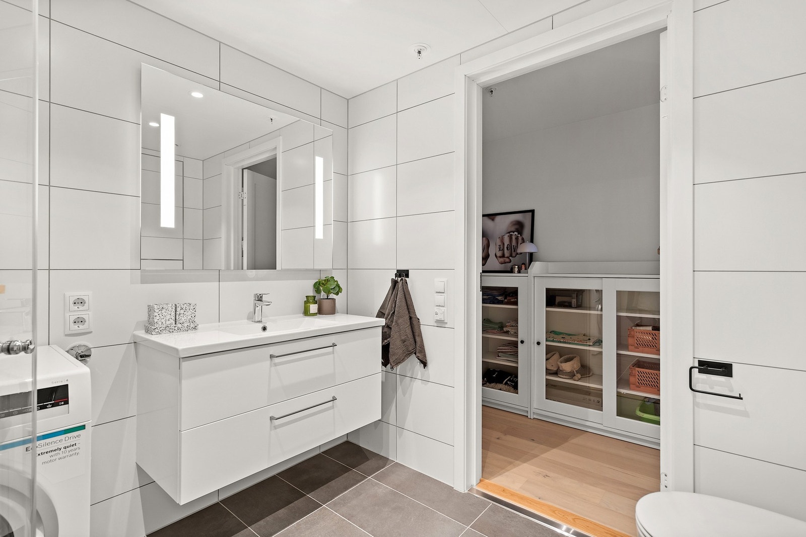 Badet er utstyrt med servant med innredning, veggmontert toalett, dusjløsning og opplegg for vaskemaskin. Et funksjonelt og delikat bad som dekker alle behov i hverdagen. Galleribilde