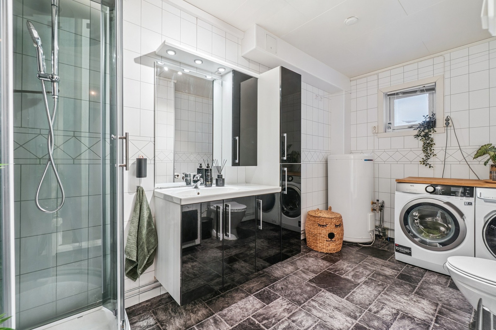 Badet har en praktisk beliggenhet ved 2 av soverommene, og fremstår tidløst og romslig med en kombinert mørk og lys utførelse på gulv, vegger og innredning. Galleribilde