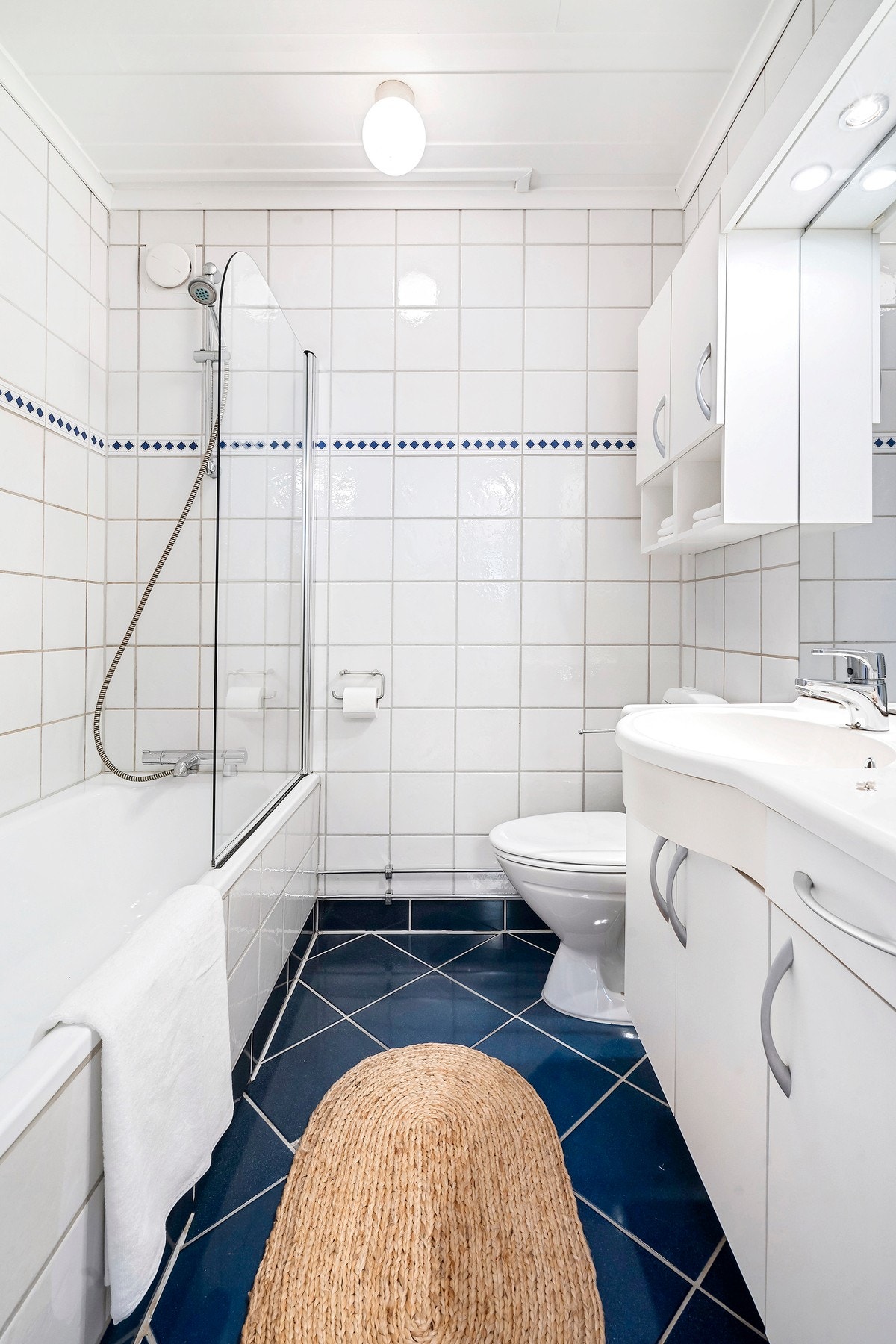 Flislagt bad med badekar og gulvstående toalett. Mye lagringsplass i baderomsinnredningen. Speil med overlys. Galleribilde