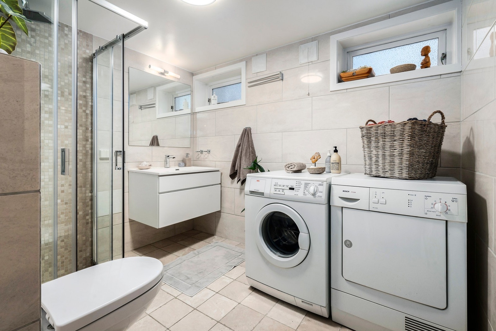 Lyst og delikat bad/vaskerom med dusjhjørne og vegghengt toalett. Romslig baderomsinnredning med speil og belysning. Galleribilde