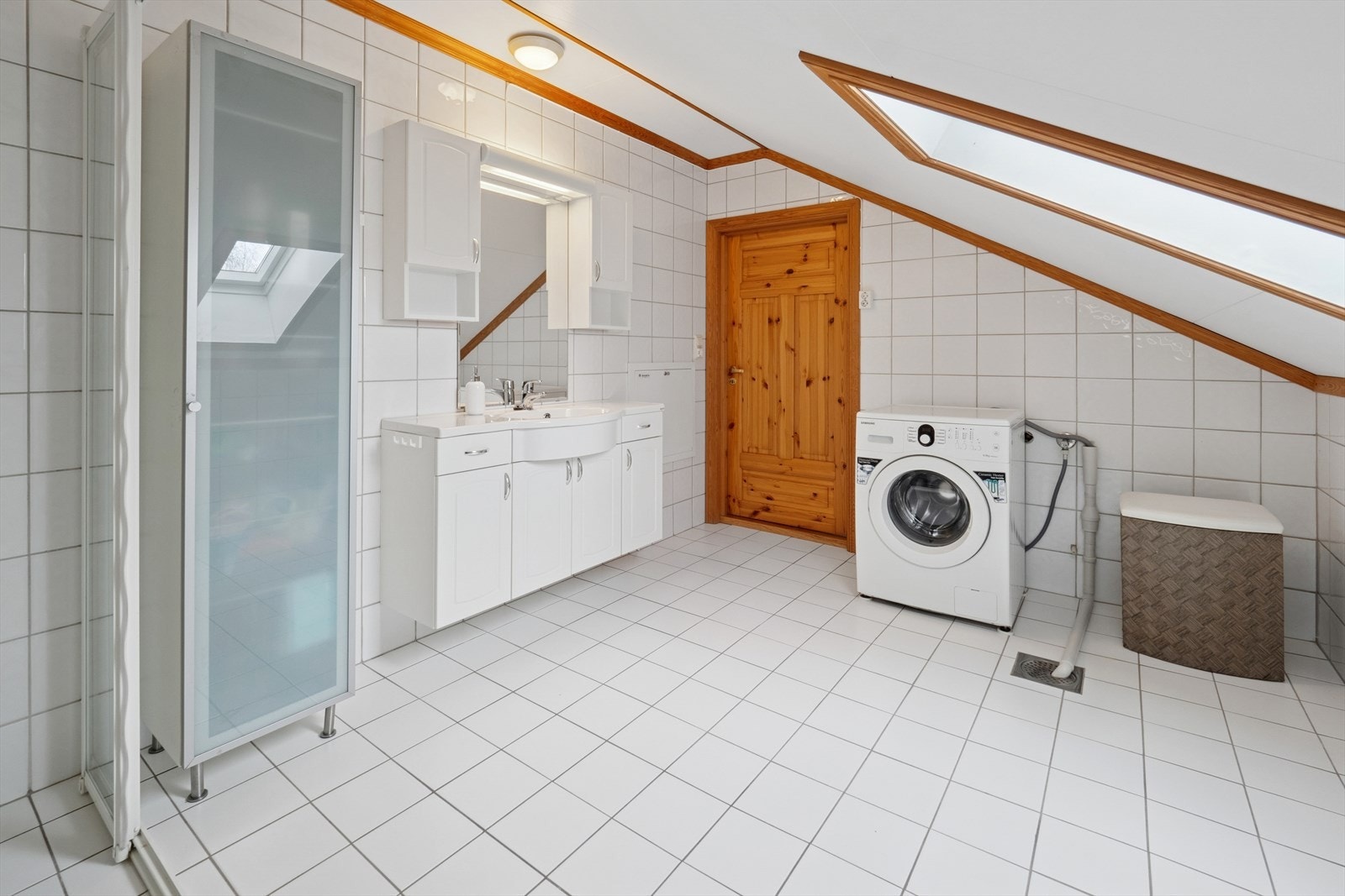 Rommet har servant, servantskap med malte profilerte fronter, gulvmontert toalett, dusjdører i herdet glass og opplegg for vaskemaskin. Galleribilde