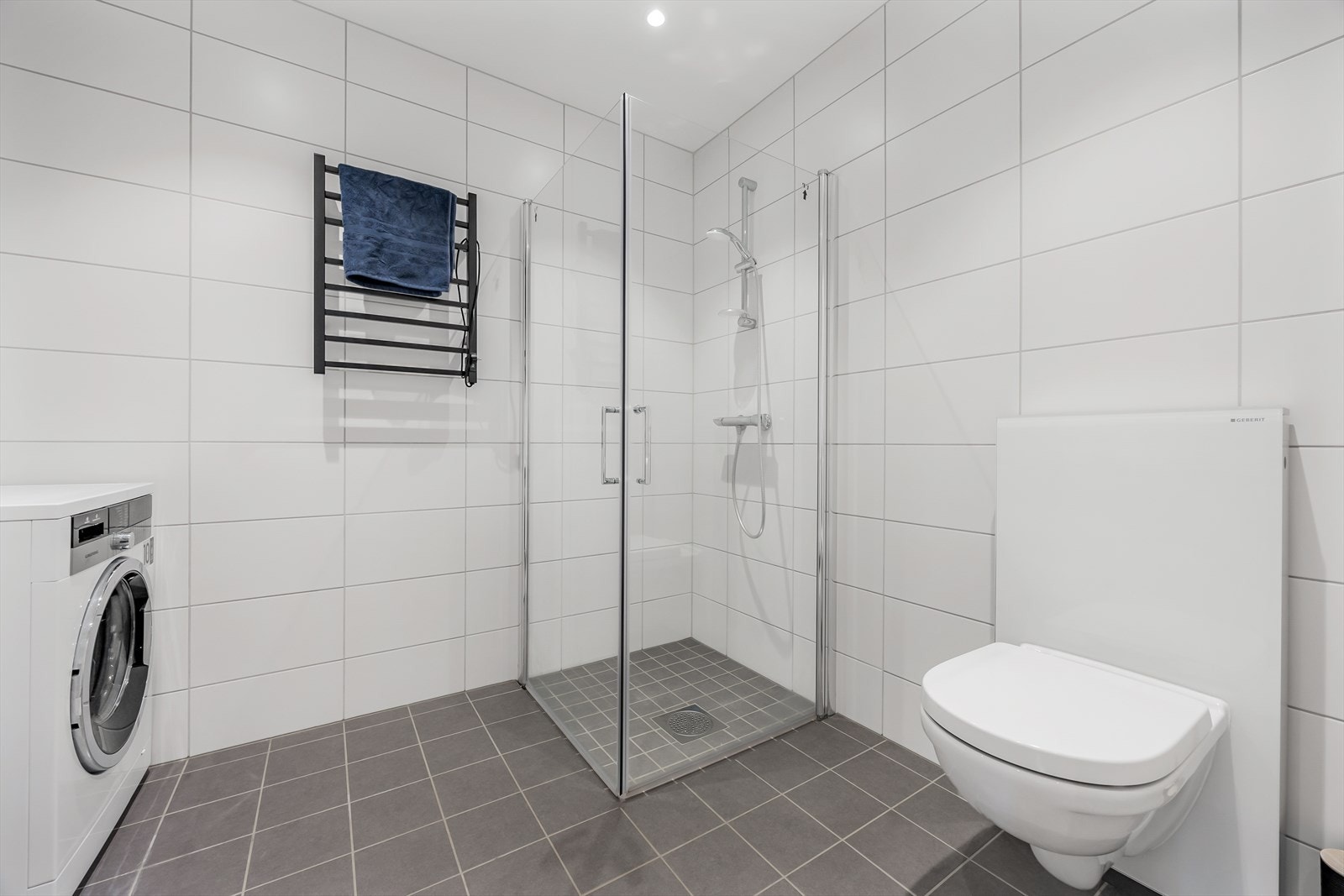 Badet er innredet med vegghengt toalett, servant i baderomsinnredning og dusjhjørne med innfellbare glassvegger. Galleribilde