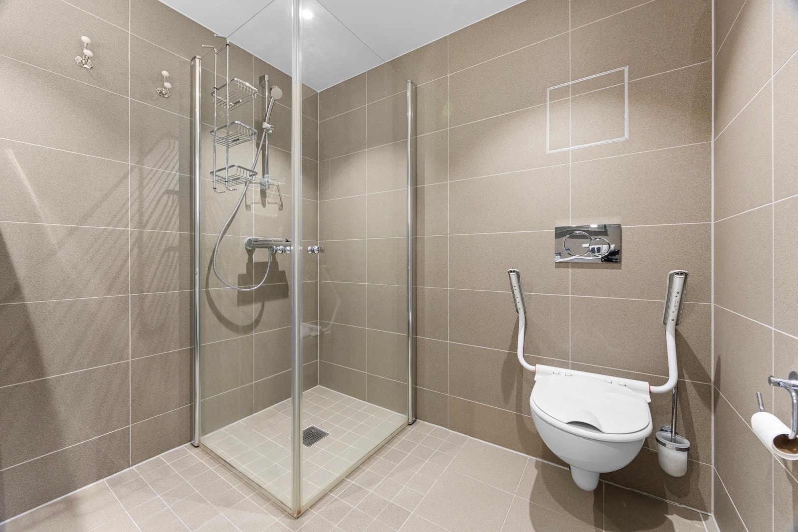 Videre er det vegghengt toalett og dusjhjørne med hånddusj og innfellbare dusjvegger i glass. Rommet har opplegg og plass for både vaskemaskin og tørketrommel. Galleribilde