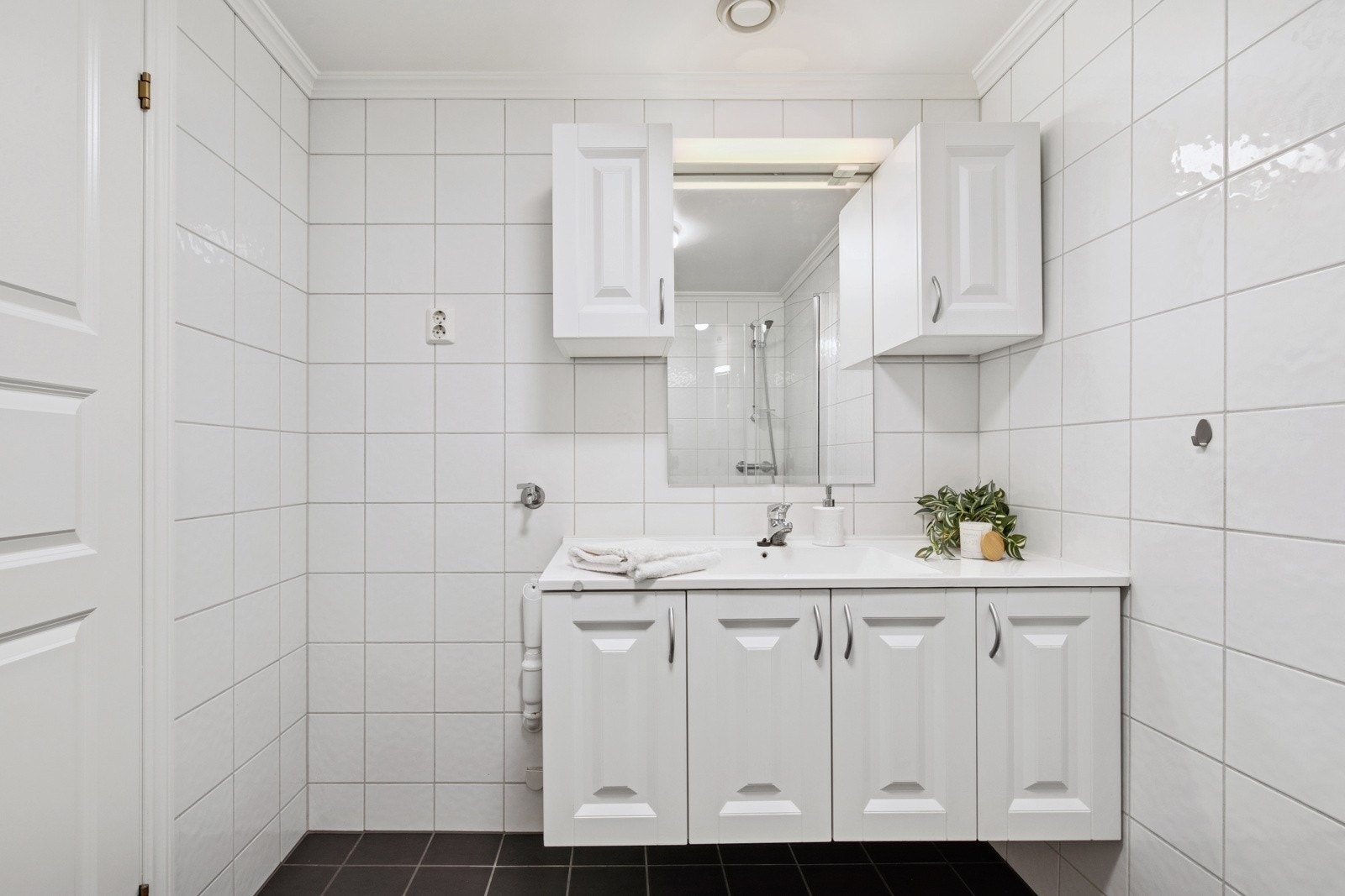 Badet er lyst, pent og er innredet med servant over servantskap med profilerte fronter, nytt dusjkabinett, klosett og opplegg til vaskemaskin. Galleribilde