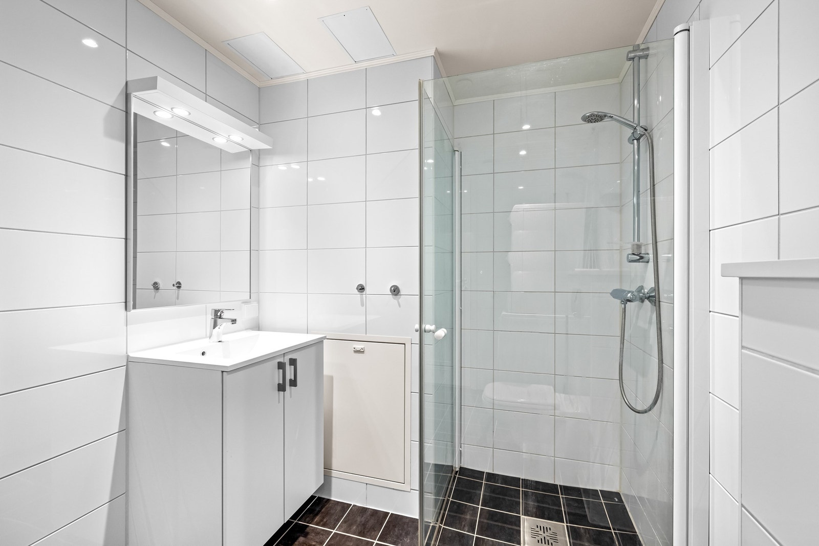 Badet er innredet med servantskap med heldekkende servant, dusjhjørne med innfellbare glassdører og vegghengt toalett. Galleribilde