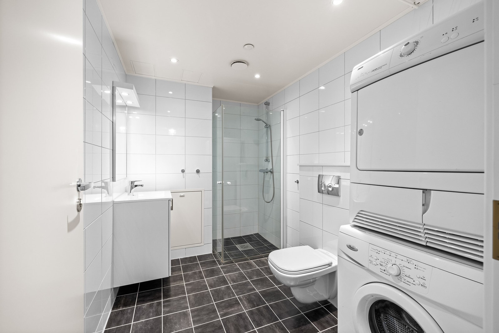 Flislagt baderom av god størrelse med plass og opplegg for både vaskemaskin og tørketrommel. Galleribilde