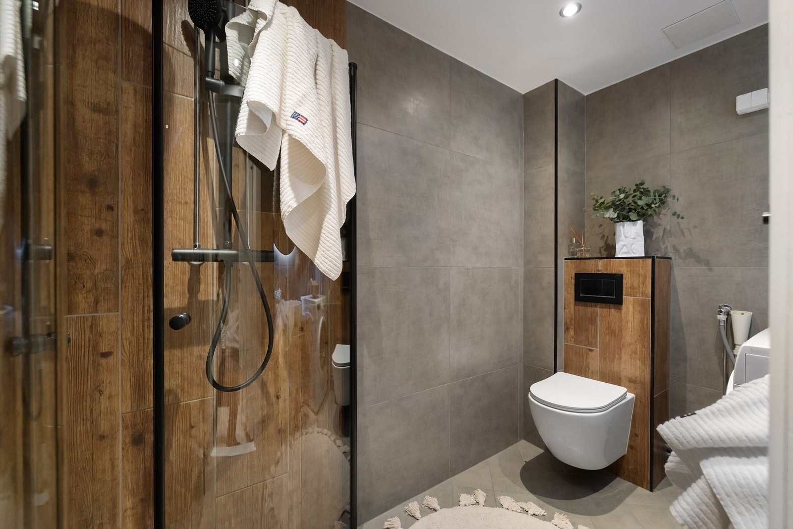 Badet er utstyrt med vegghengt toalett, dusjhjørne med innfellbar glassdører og dusjsett med rainshower, begge i sort utførelse Galleribilde