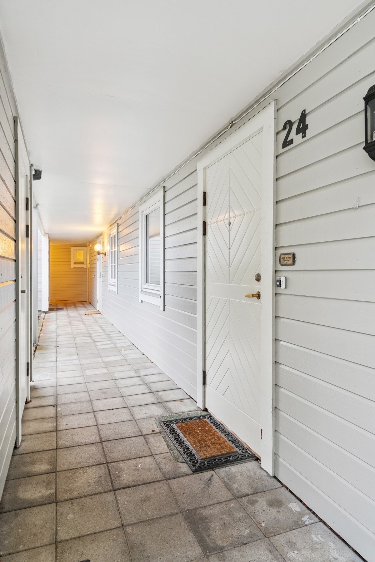 Entré med overbygg og belysning på veggen. Vis a vis inngangen er det en utvendig bod tilhørende leiligheten. Galleribilde