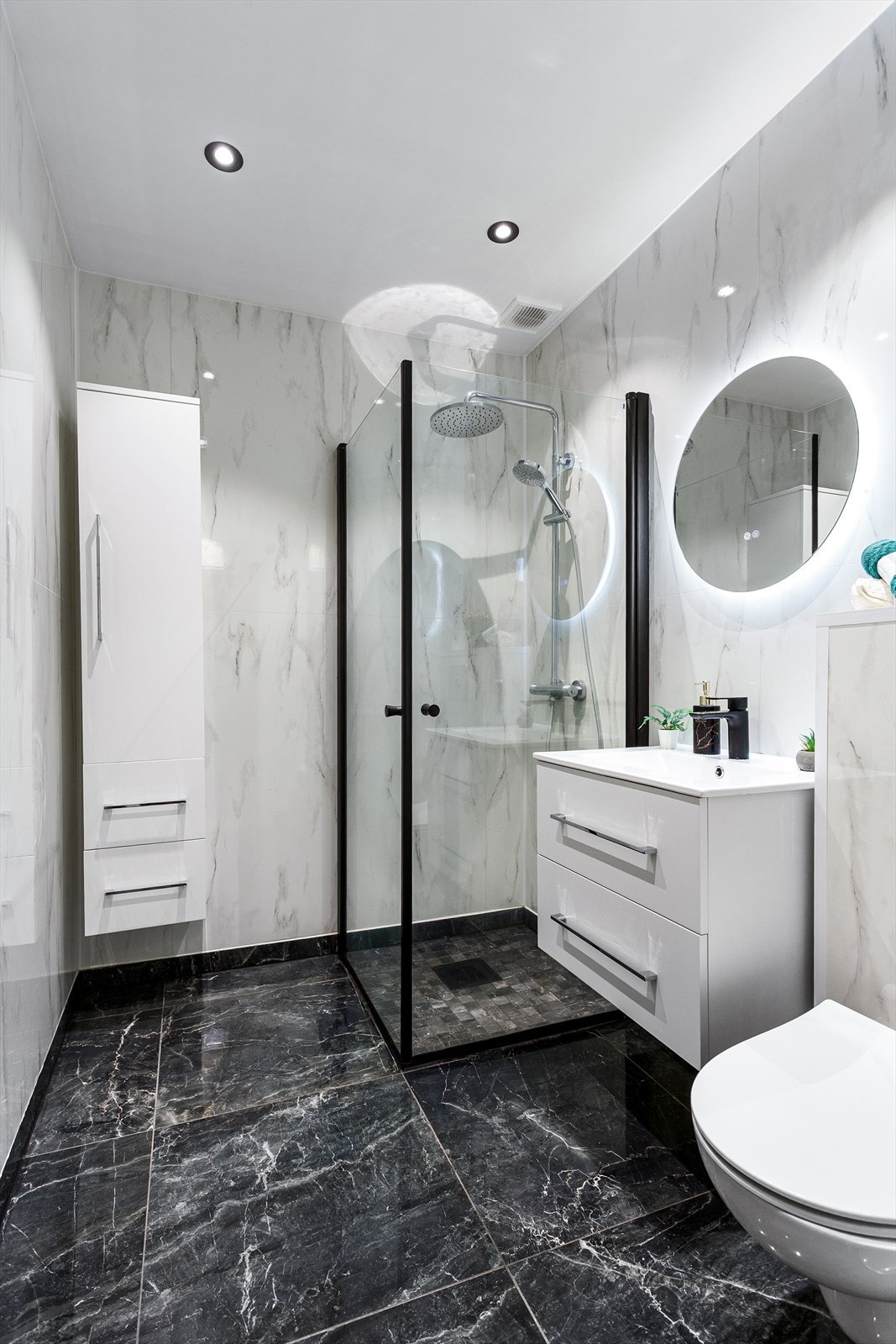 Badet er videre utstyrt med pen innredning har rom for oppbevaring i skuffeseksjon, høy skap, trendy rundt speil, vegghengt toalett og dusjhjørne. Galleribilde