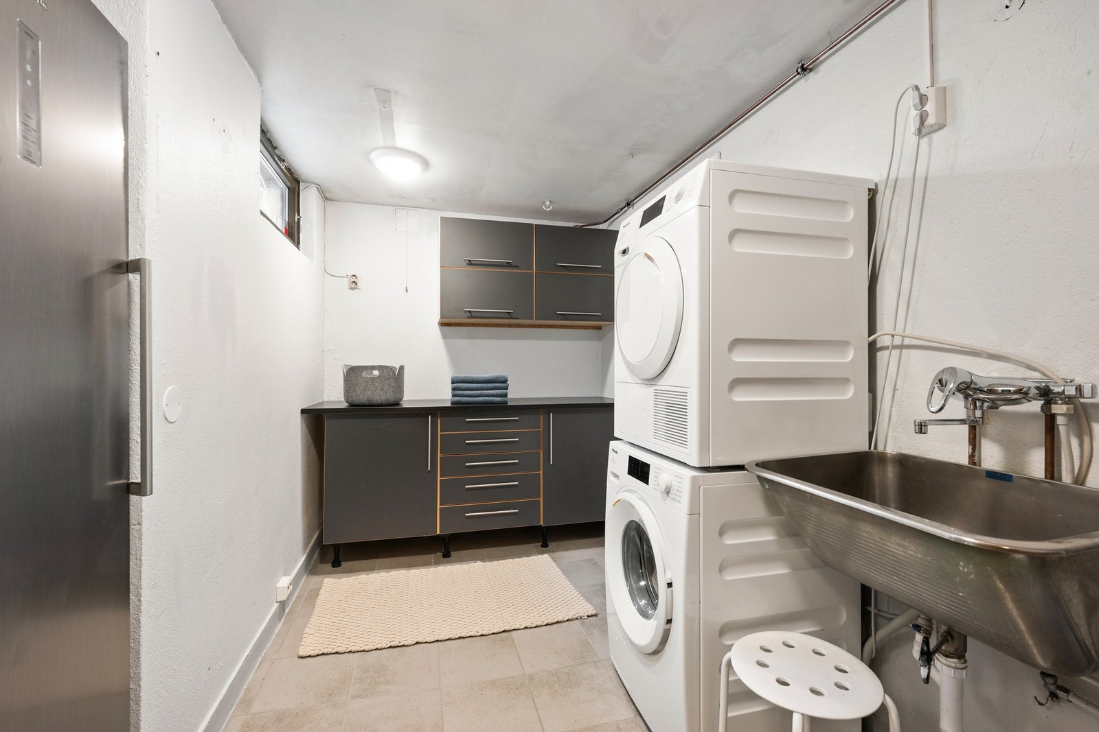 Praktisk vaskerom i underetasjen med flislagt gulv, opplegg for vaskemaskin og tørketrommel samt utslagsvask. Galleribilde