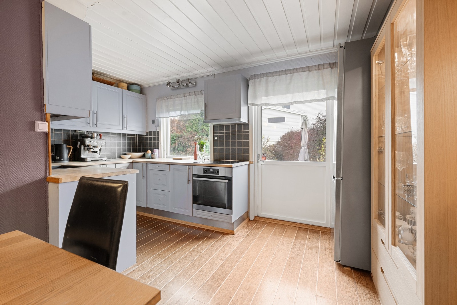 Store vindusflater gir godt lysinnslipp og utsyn til hagen, og en praktisk dør fører direkte ut til hage og terrasse - perfekt for servering på varme sommerdager. Galleribilde