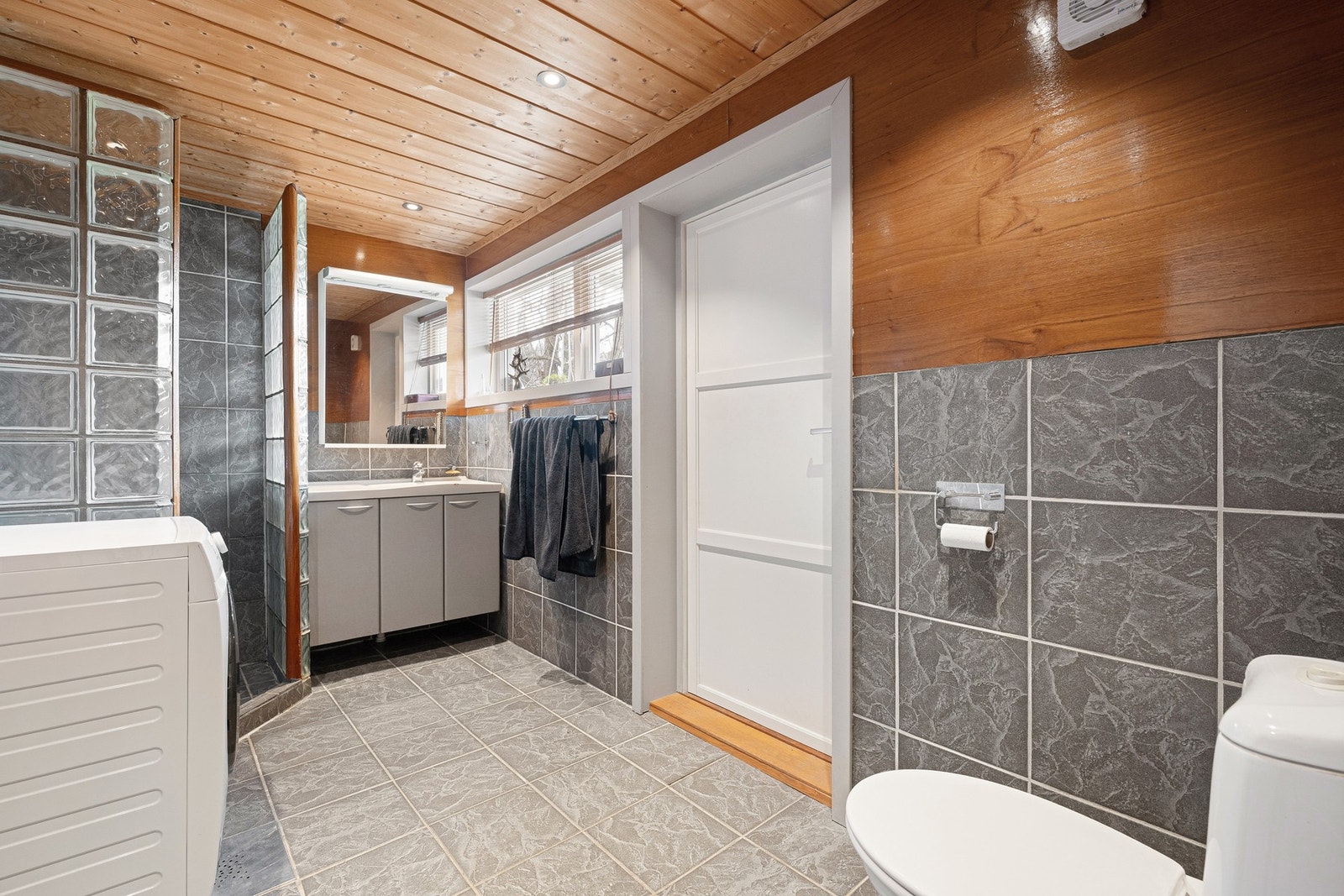 Rommet har flislagt gulv med varme, flislagte og finérkledde vegger samt nedforet himling med downlights som gir et behagelig lys. Det er opplegg for vaskemaskin. Galleribilde