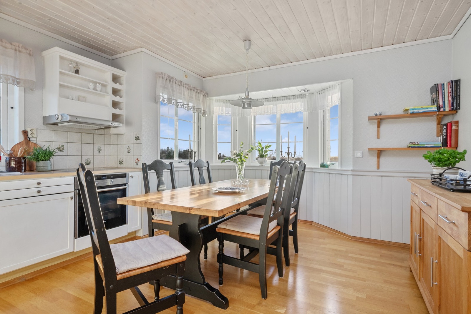 Et karnapp bidrar med mye naturlig lys til matlagingen. Innredningen har hvite, profilerte fronter, vinhyller, nedfelt oppvaskkum og benkeplate av laminat. Galleribilde