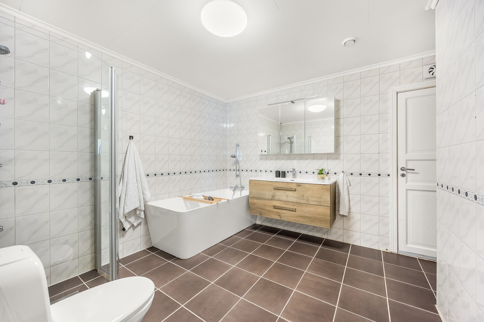 Fint helfliset bad med varmekabler i gulv. Dusjhjørne, badekar, vask i seksjon og speilskap med belysning. Galleribilde