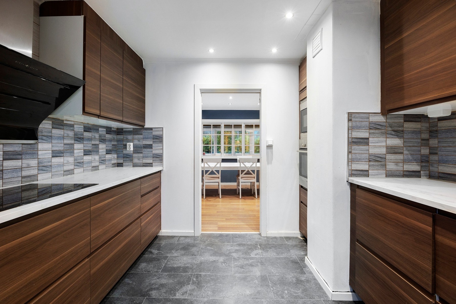 Videre er kjøkkenet innredet med integrerte hvitevarer som kombiskap, oppvaskmaskin, komfyr, mikrobølgeovn og platetopp Galleribilde