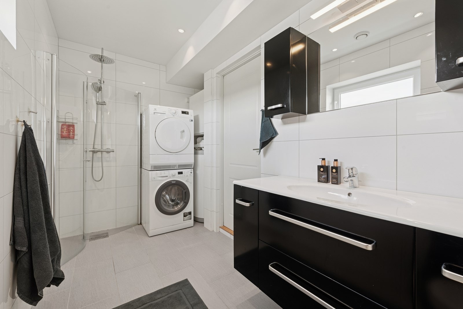 Flislagt baderom i 1. etasje med behagelige varmekabler i gulvet, utstyrt med toalett, dusjhjørne med glassdører, baderomsinnredning og opplegg for vaskemaskin. Galleribilde