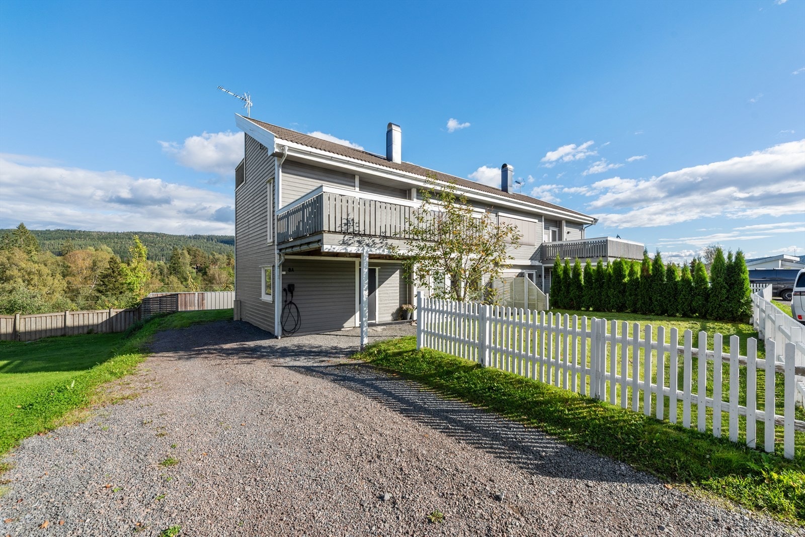 Gruset gårdsplass med gode parkeringsmulighter. Det er el-bil lader montert på husveggen. Galleribilde