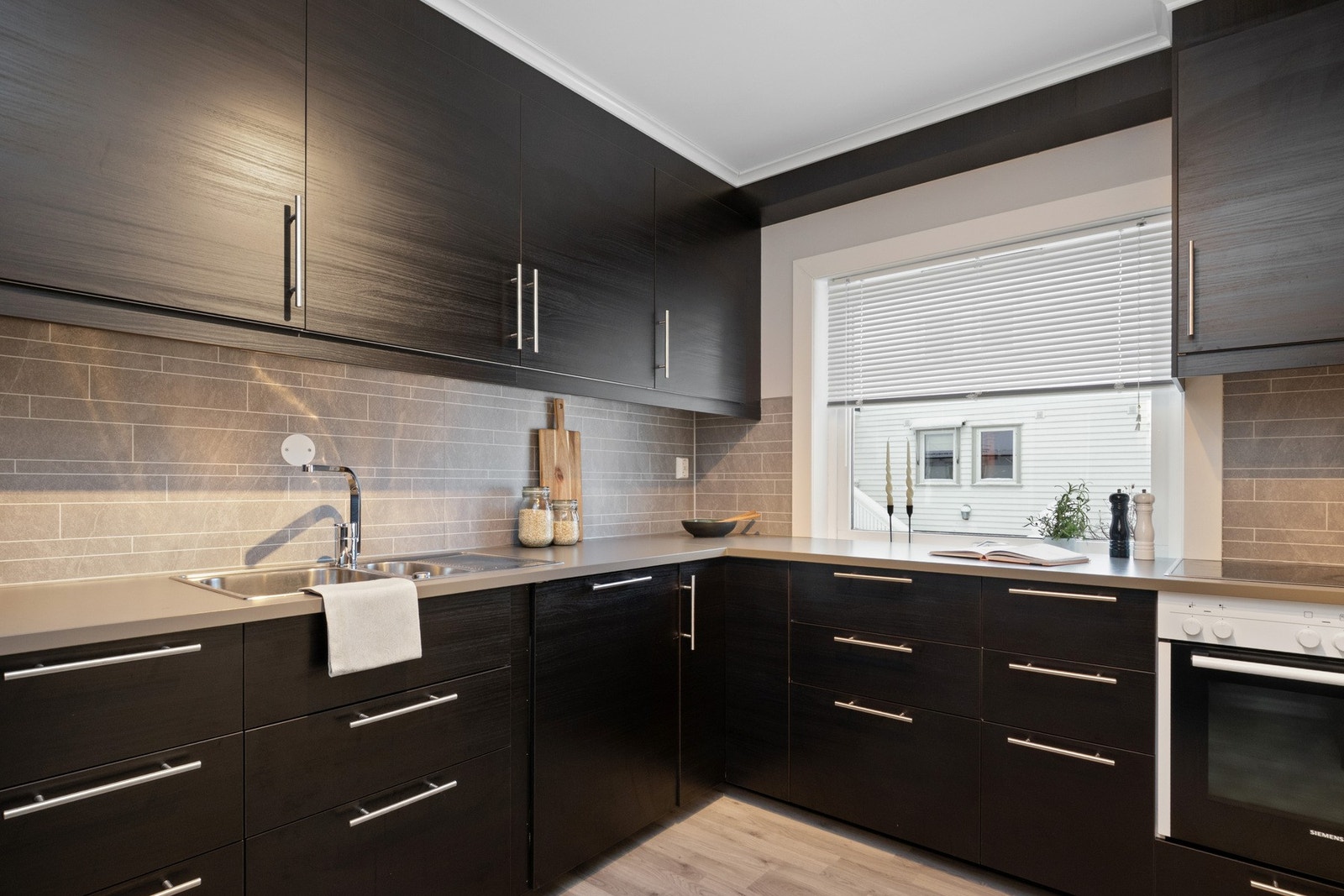 Over benken er det lysegrå plater i flismønster, og over kokesonen har kjøkkenet en ventilator med avtrekk ut. Galleribilde