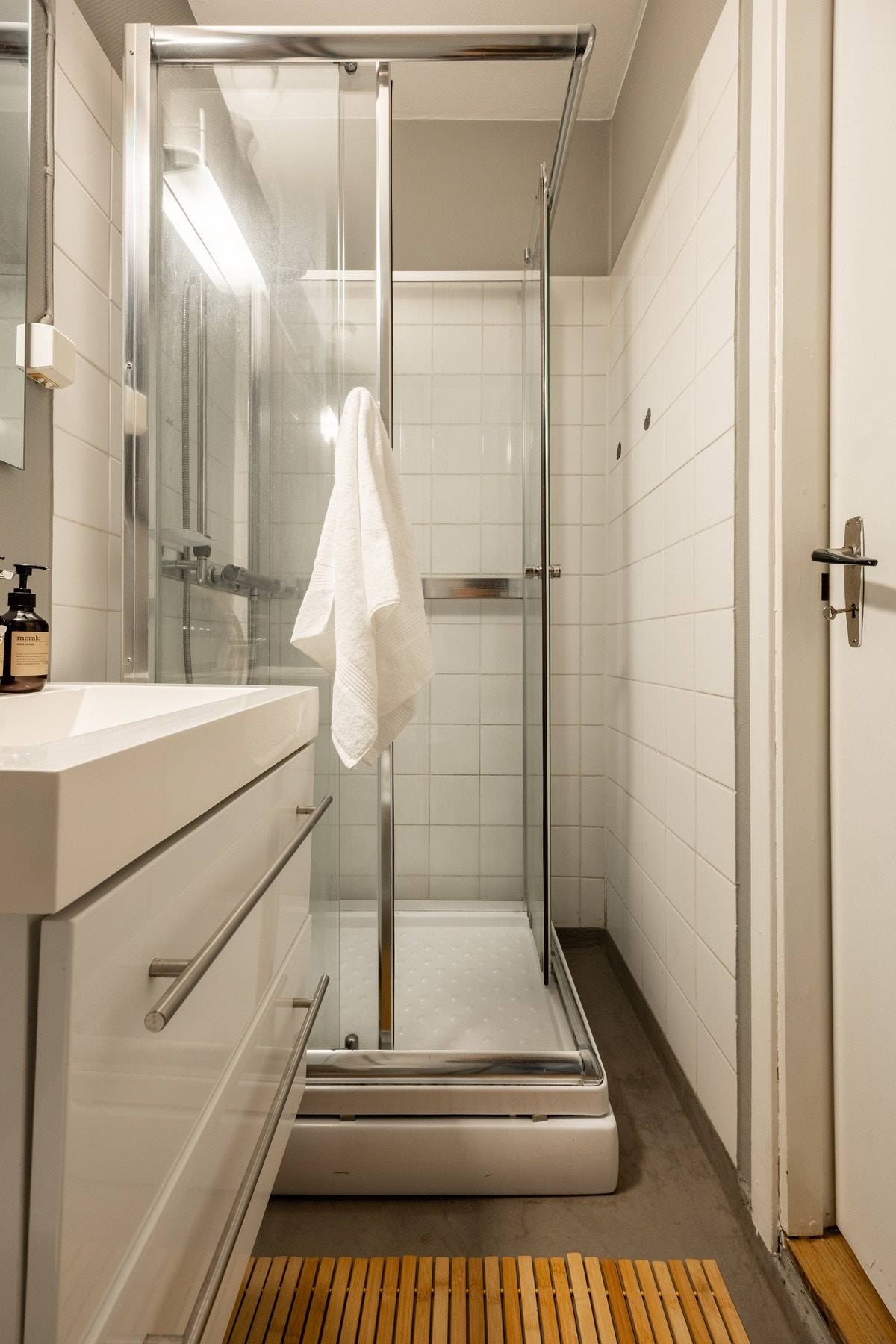 Badet er innredet med vegghengt servantinnredning med skuffer og ovenpåliggende servant med ett-greps armatur, speil, overlys og stikkontakt på vegg over servant, dusjkabinett med dusjarmatur, samt gulvstående toalett. Galleribilde