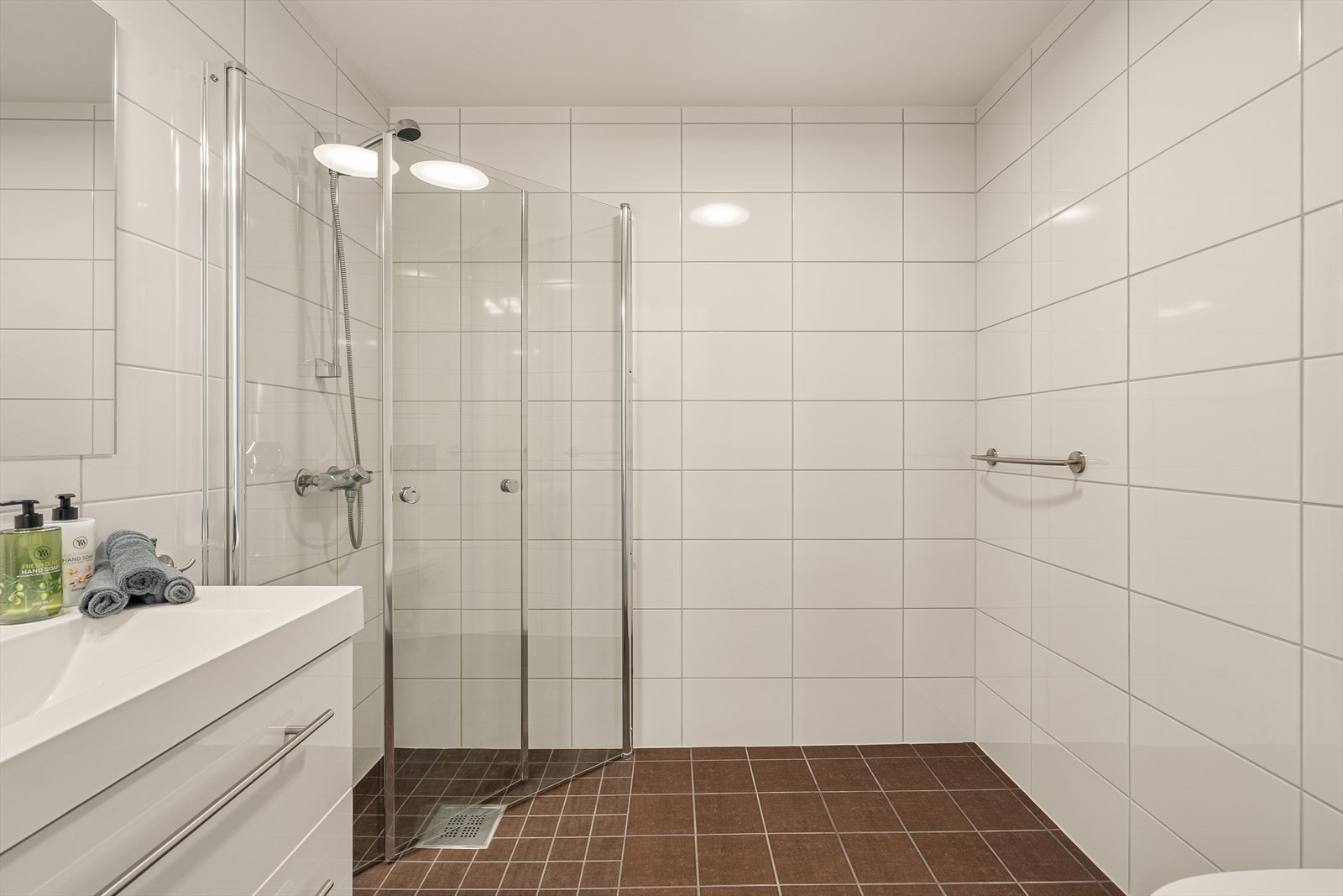 Badet i 1. etasje. Keramiske fliser på gulv og vegger. Utstyrt med vegghengt toalett, dusjhjørne og heldekkende servant. Galleribilde