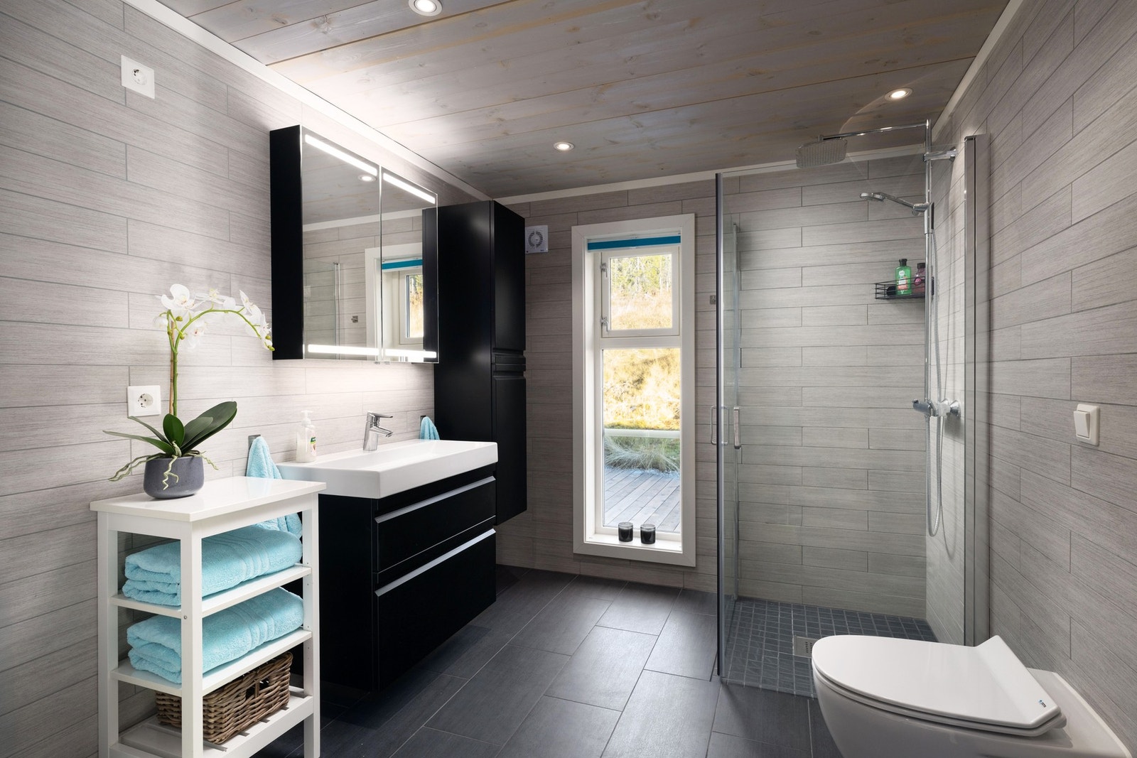 Badet har fliser på gulv og vegg, og varmekabler i gulvet. Innredet med dusjnisje, servantinnredning, vegghengt høyskap, vegghengt Jets vannklosett. Opplegg for vaskemaskin og tørketrommel. Galleribilde