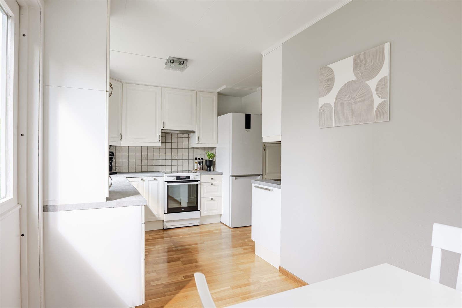 Innnredningen har profilerte fronter og laminert benkeplate med nedfelt oppvaskkum. Praktisk med fliser i benkeryggen og belysning under de takhøye overskapene. Galleribilde