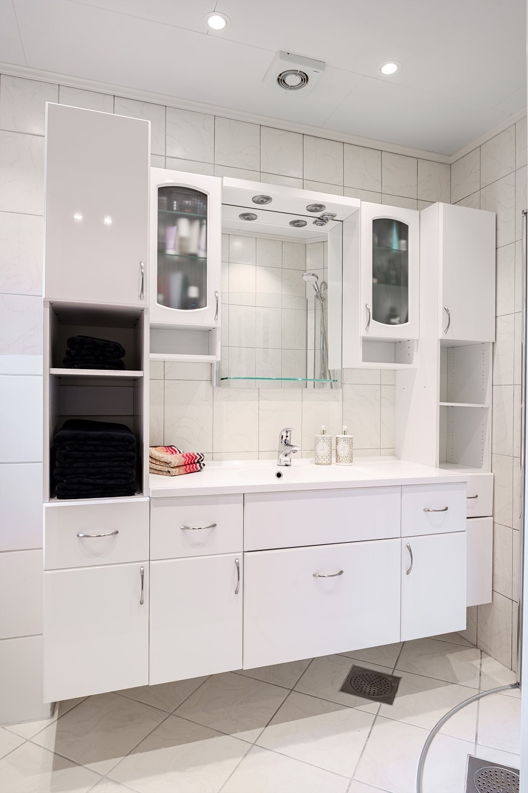 Lys baderomsinnredning med god oppbevaringsplass, heldekkende servant, speil med glasshylle og belysning over. Galleribilde