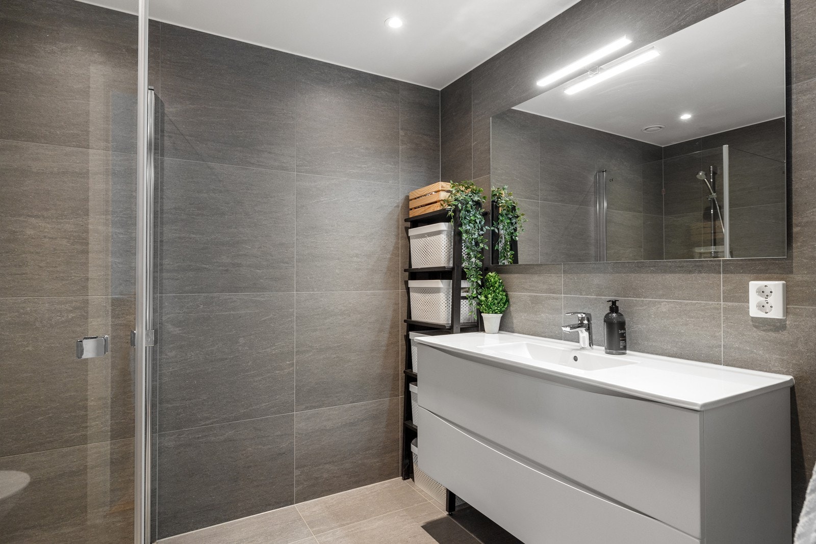 Badet er innredet med servant i baderomsinnredning, speil med belysing, vegghengt toalett og dusjhjørne. Galleribilde