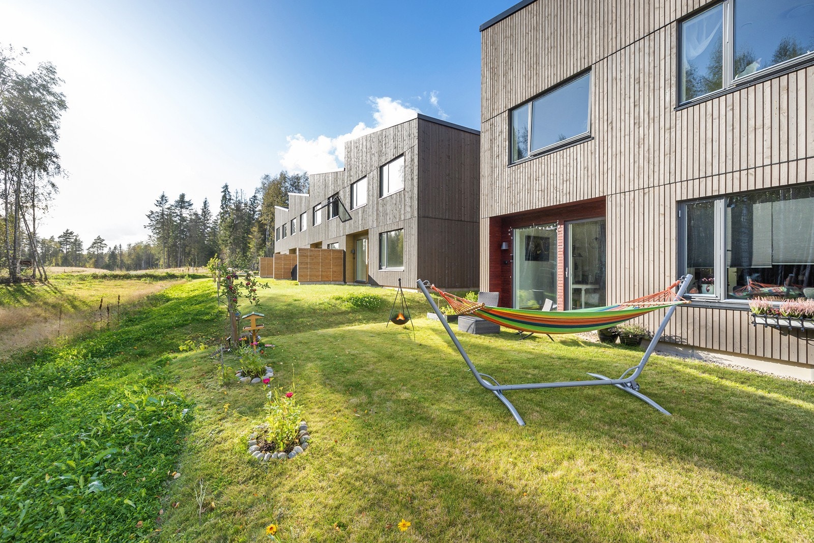 Koselig hage i bakkant som er opparbeidet med plen, beplanting og et hyggelig uteområde. Galleribilde