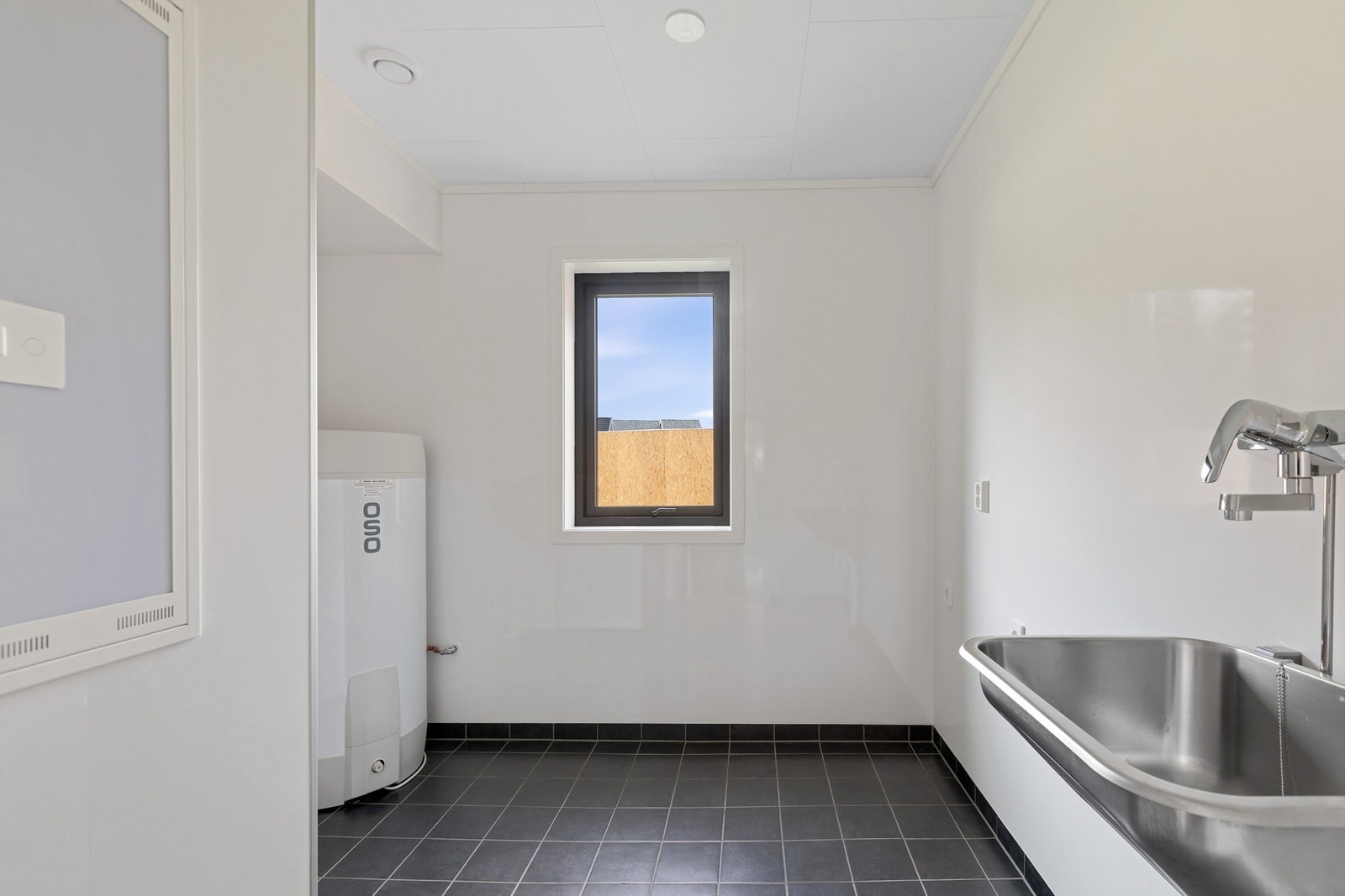 Vaskerom med opplegg vaskemaskin, utslagsvask og varmtvannsbereder. Fliser på gulv Galleribilde