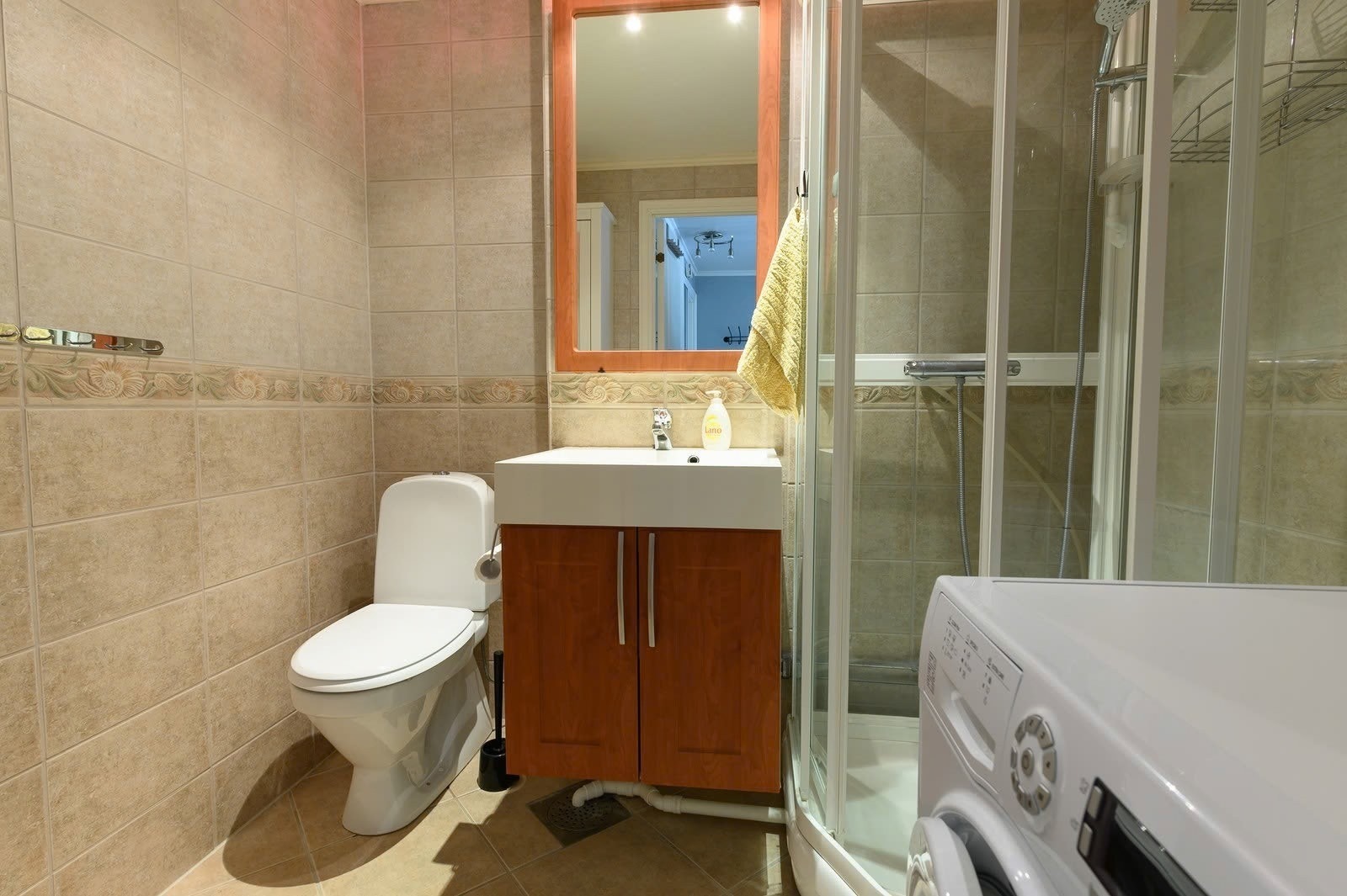 Lyst fint bad med toalett, dusj og innredning med vask og speil, samt vaskemaskin. Galleribilde