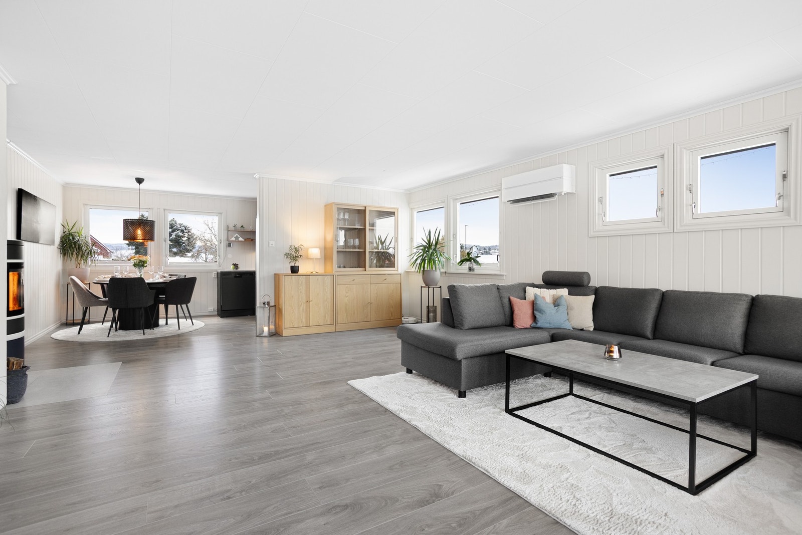 Stuen og kjøkkenet danner et åpent, luftig og innbydende allrom med klart avdelte soner. Med både peisovn og varmepumpe får man det lunt og godt i stuen. Galleribilde