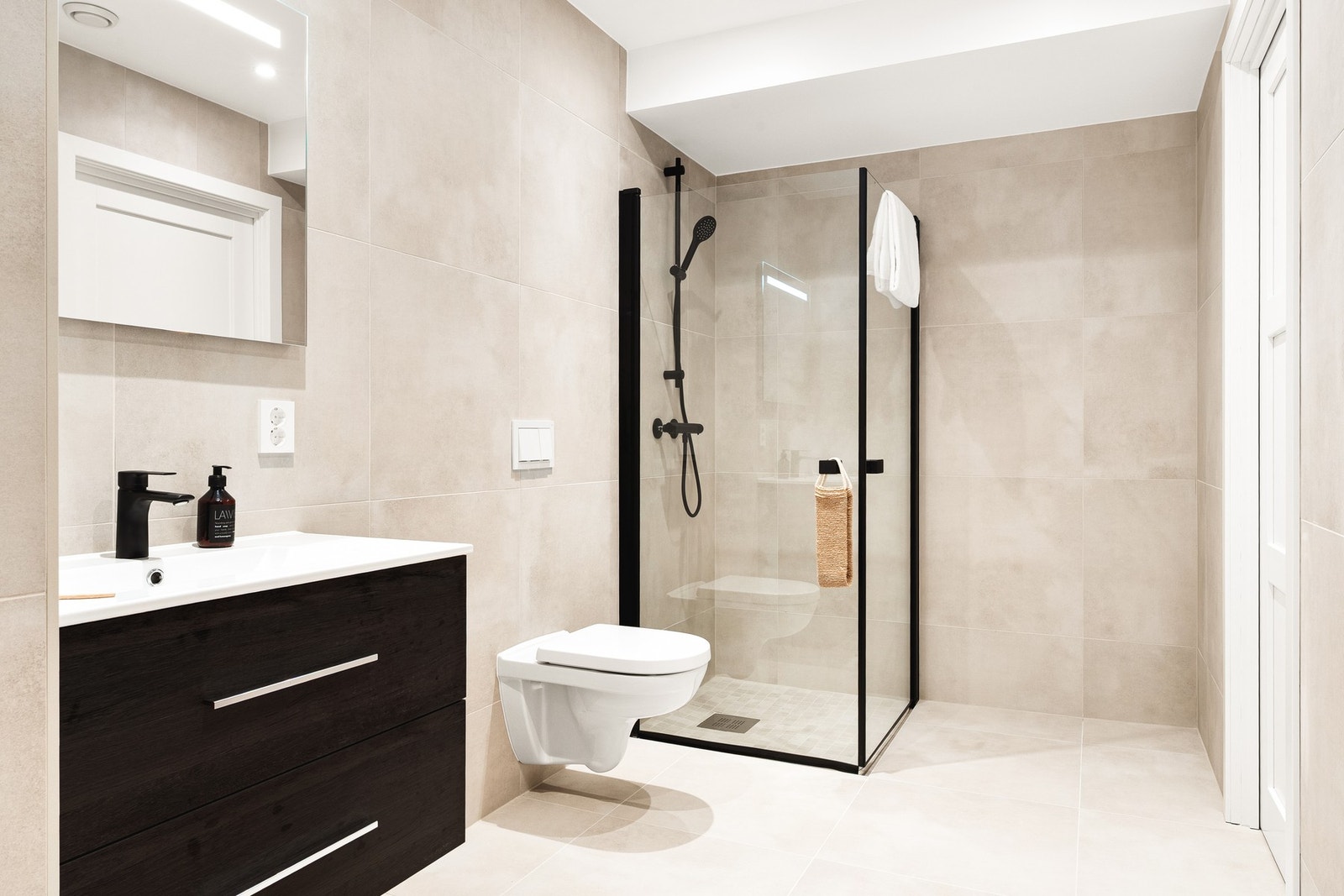 Begge badene er helflisede med moderne fargetoner, sorte detaljer, dusjhjørne og varmekabler i gulv. Galleribilde