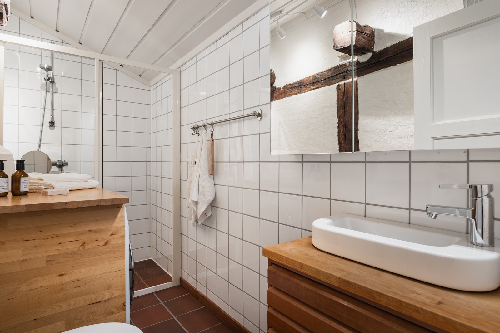 Funksjonelt, flislagt bad i hovedetasjen med dusj, servantskap med trespiler og opplegg for vaskemaskin. Galleribilde