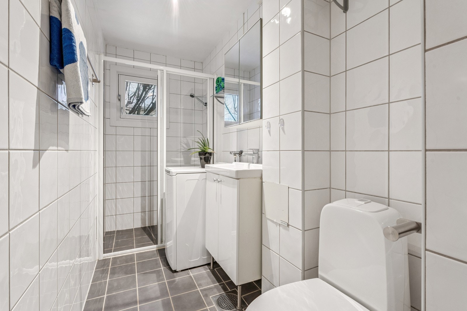 Badet inneholder toalett, servant med skap under, speilskap og dusj i hjørne med skyvedør. Galleribilde