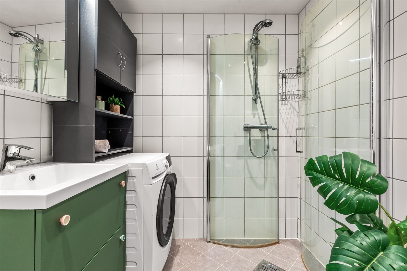 Badet har et praktisk dusjhjørne og er belagt med fliser på både gulv og vegger. Moderne og gjennomtenkte fargevalg gir et stilrent og tidsriktig uttrykk. Galleribilde