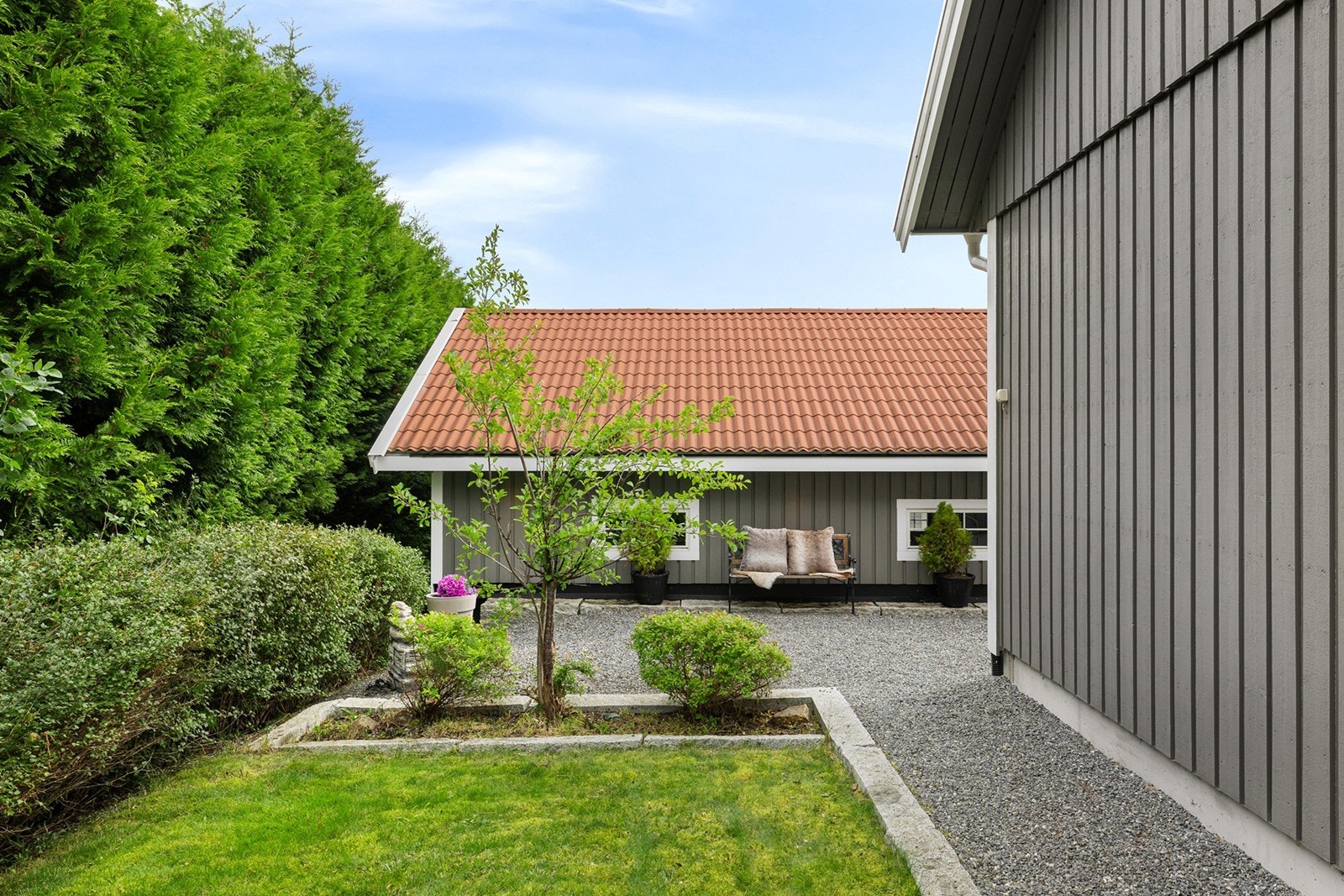 En innbydende og skjermet hagekrok med flott beplantning, grønn hekk og gruslagt gårdsplass. Galleribilde