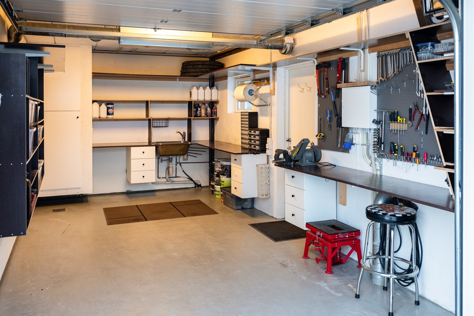Enkelt garasjen er i dag også brukt som hobbyrom, her er det etablert skyllekum, uttak til vaskemaskin, tørkeskap og varme i gulv. Galleribilde